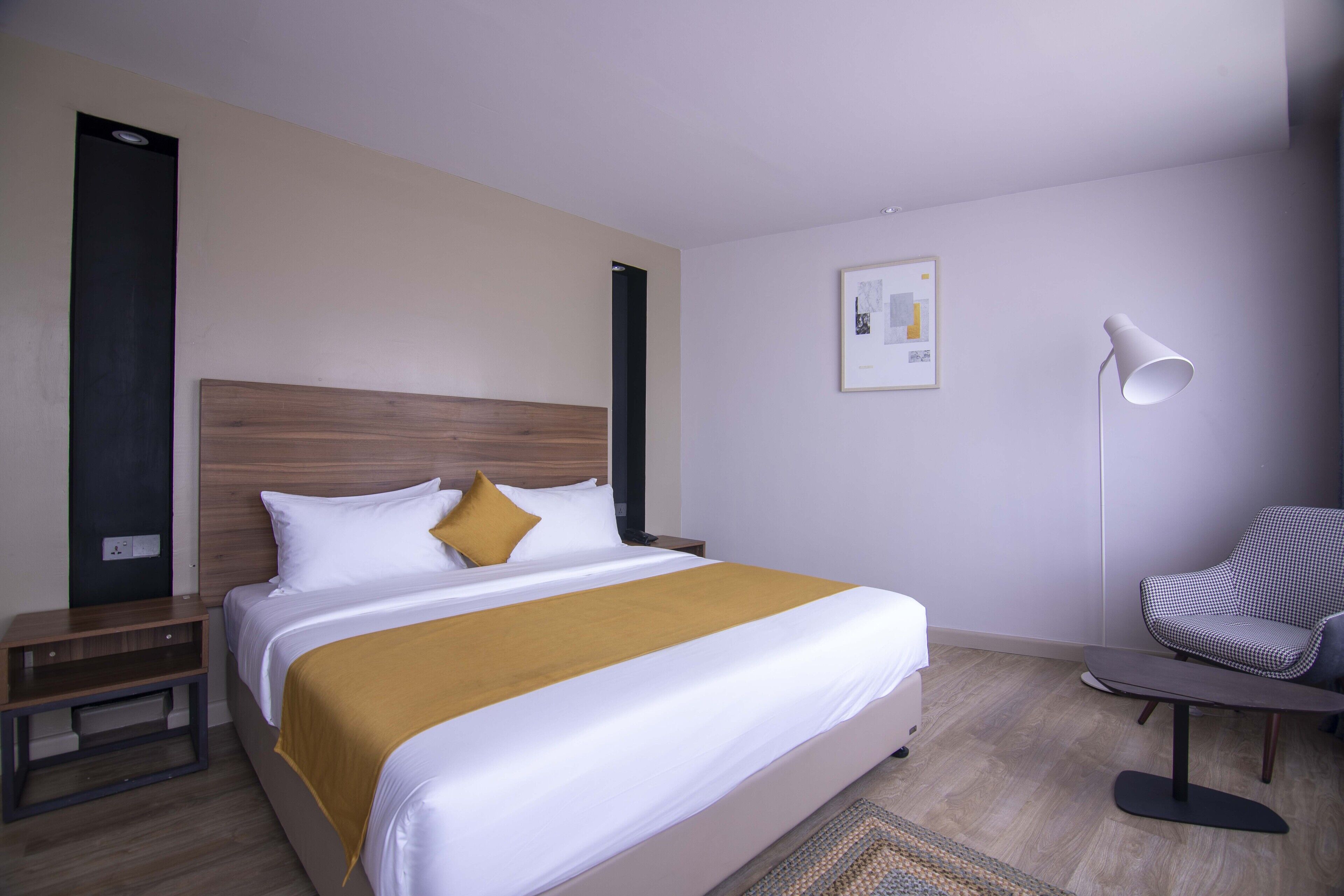 A modern hotel room with a large bed, a bedside table, a chair, and a floor lamp.
