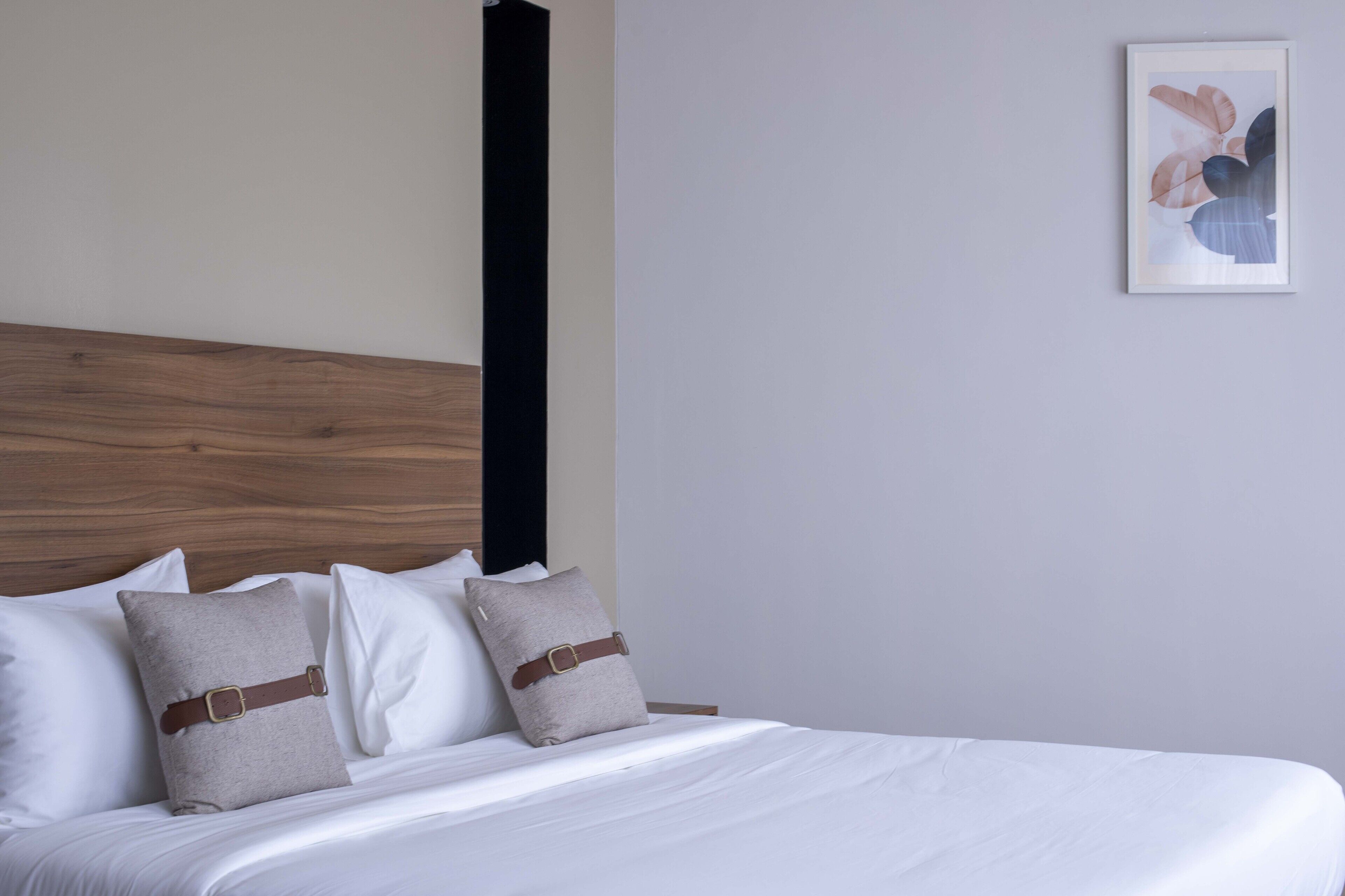 A neatly made bed with white linens and two pillows, one with a brown belt.