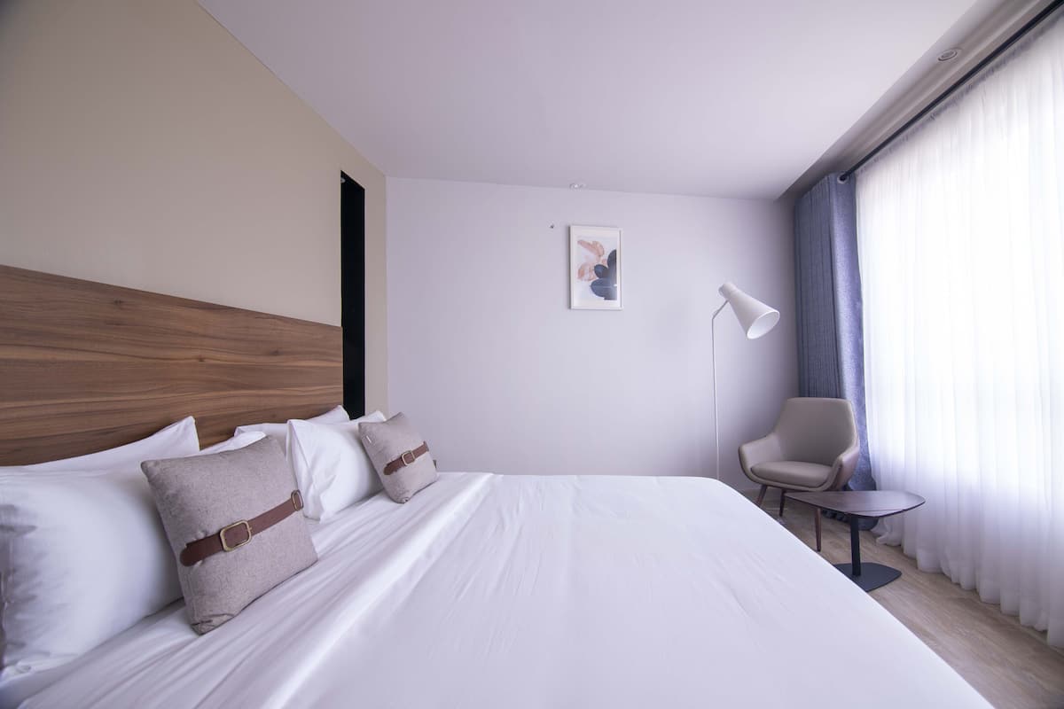 A hotel room with a large bed, a chair, a desk, and a picture on the wall.
