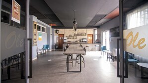 A spacious, modern interior with a long communal table, seating areas, and a kitchen in the background.