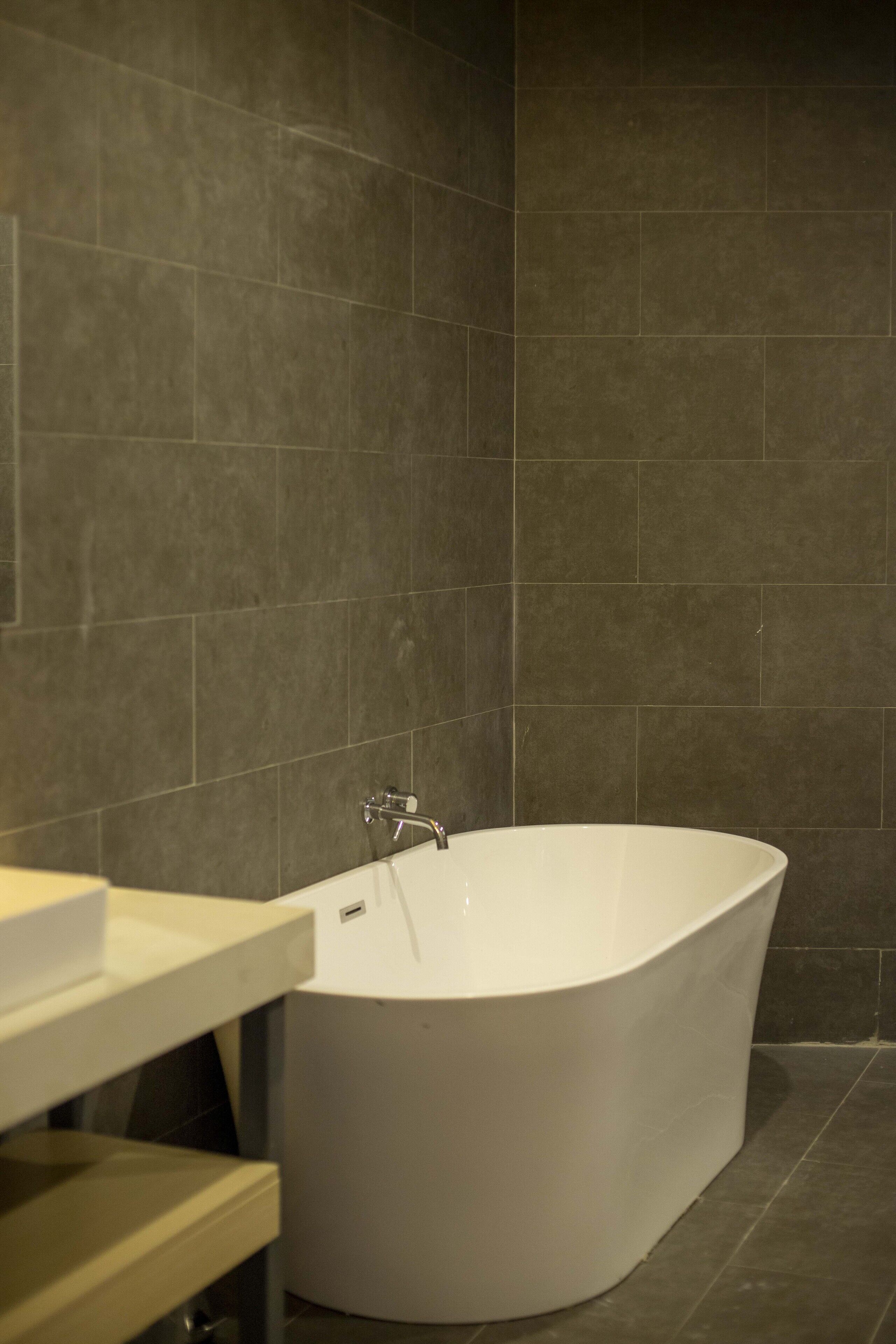 Un baño moderno con una bañera independiente, un tocador con espejo y paredes de azulejos oscuros.
