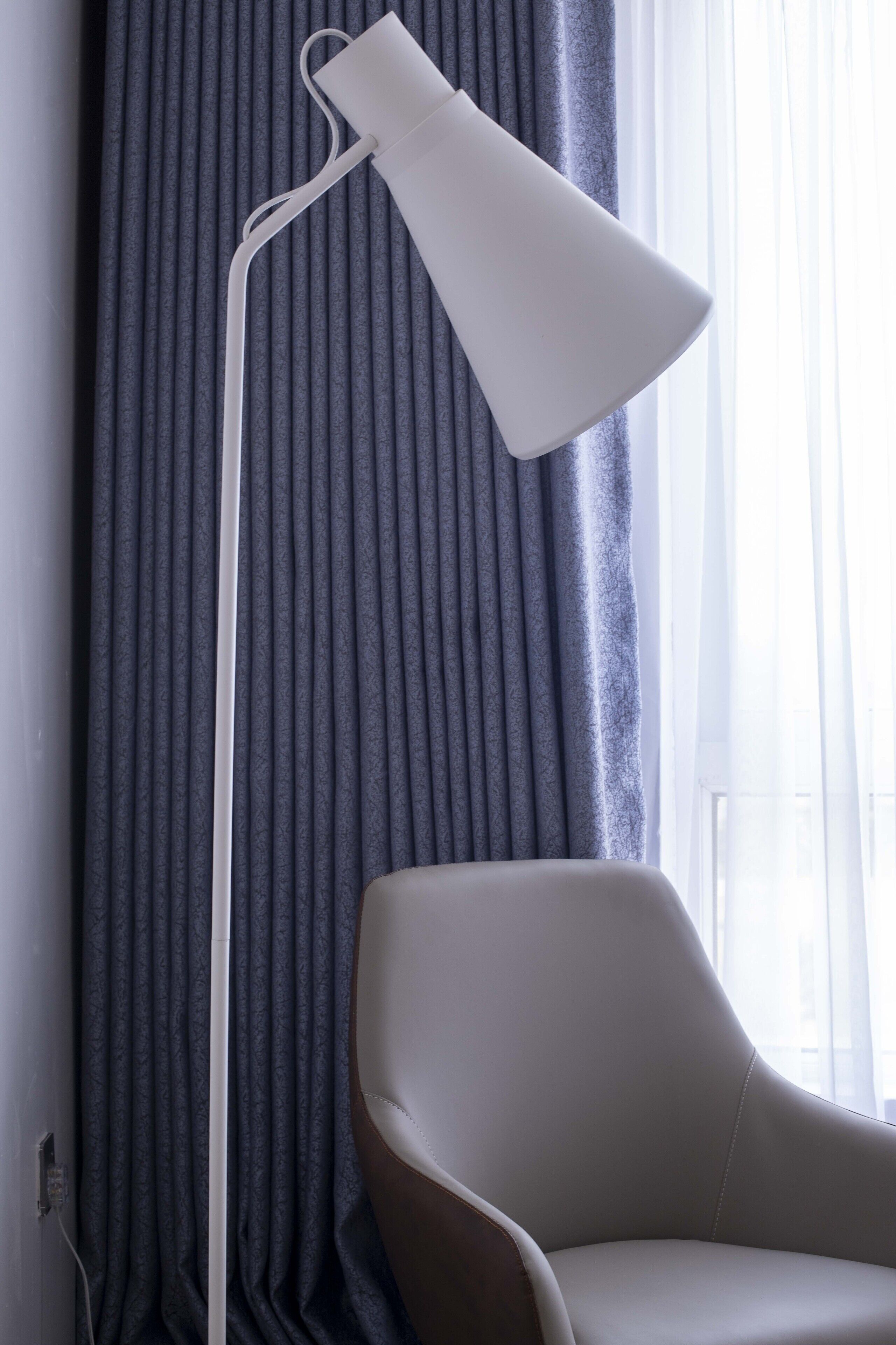 A modern room with a floor lamp, a chair, and a window with curtains.