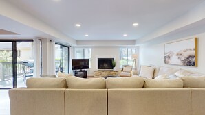 Amplia sala de estar con un sofá seccional beige grande, un televisor de pantalla plana, una chimenea y un ventanal con vistas al exterior.