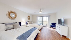 Un dormitorio moderno con dos camas, ventilador de techo, televisión y balcón.