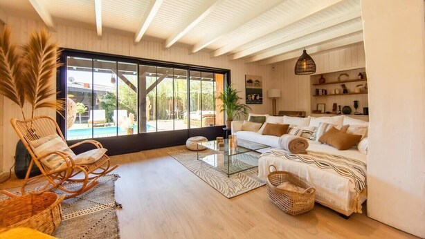 A spacious living room with a large window, a white sofa, a glass coffee table, and a wicker chair.