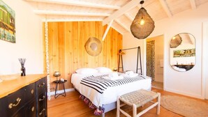 A bedroom with a wooden ceiling, a bed with white bedding, a bedside table, a lamp, and a mirror on the wall.