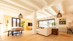 A spacious living area with a dining table, sofa, and a large window providing natural light.