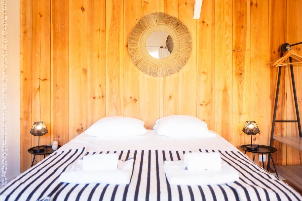 Una habitación con paneles de madera, una cama, dos mesitas de noche, un espejo y un perchero.