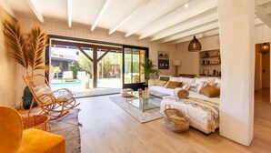 A spacious living room with a large glass door leading to an outdoor area, a sofa set, a coffee table, and a wicker chair.
