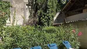 Eine Terrasse mit blauen Lounge-Stühlen und weißen Kissen, umgeben von Grünpflanzen und einer Steinmauer.