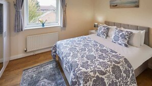 Une chambre avec un grand lit, une fenêtre avec des rideaux, un radiateur, une table de chevet avec une lampe et un tableau au mur.