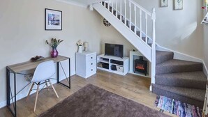 Un salon avec un bureau en bois, une chaise blanche, un meuble pour la télévision et un escalier.