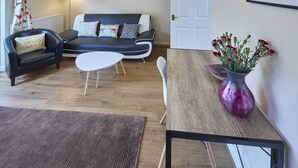 Un salon avec un canapé, une table basse, un fauteuil, un tapis et un vase de fleurs.
