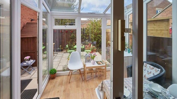 Une véranda dotée d’une porte vitrée donnant sur un patio aménagé avec une table, des chaises et un petit jardin.