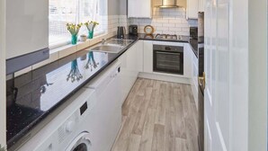 Une cuisine compacte équipée d’un lave-linge, d’un évier, d’une cuisinière et d’une fenêtre agrémentée de plantes.