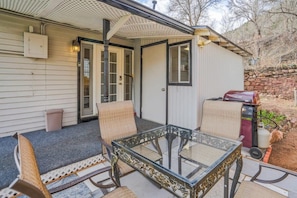 Eine Terrasse mit Glastisch, Korbstühlen, einem kleinen Schuppen und einem Grill.