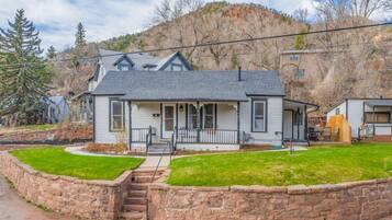 A two-story house with a stone retaining wall, a front porch, and a mountain backdrop.