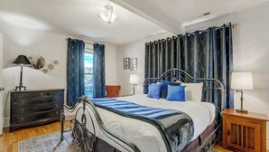 Een slaapkamer met een bed, twee nachtkastjes, een dressoir, een raam met gordijnen en een plafondlamp.