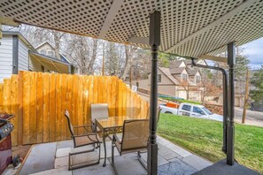 Un patio couvert, agrémenté d’une clôture en bois, de mobilier d’extérieur et offrant une vue sur une rue résidentielle.