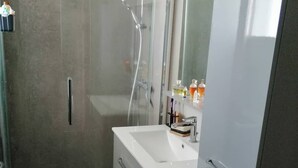 Ein modernes Badezimmer mit einer Duschkabine aus Glas, einem weißen Waschbecken mit Spiegel darüber und einem Edelstahl-Kühlschrank.