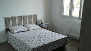 Ein Schlafzimmer mit Bett, Nachttisch, Lampe und Fenster.