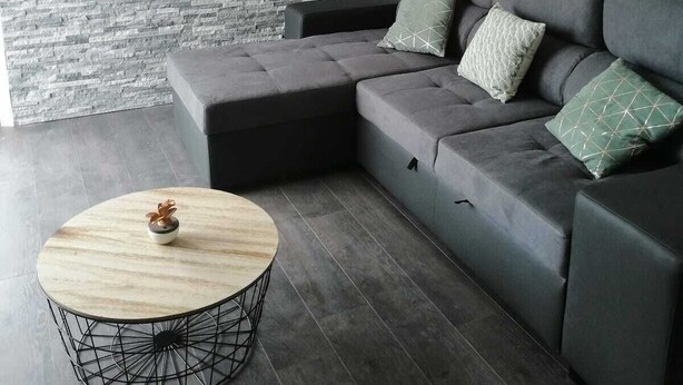 Ein modernes Wohnzimmer mit einem grauen Ecksofa, einem runden Couchtisch und einer Wand aus grauem Stein.