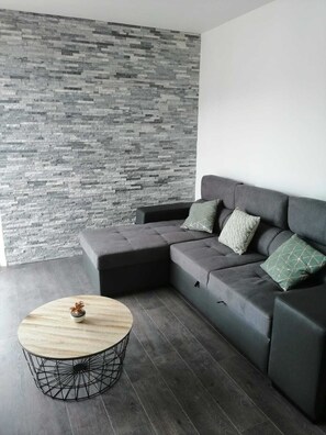A modern living room with a grey sectional sofa, a round coffee table, and a grey stone wall. - Appartement Lumineux Annecy (Annecy)