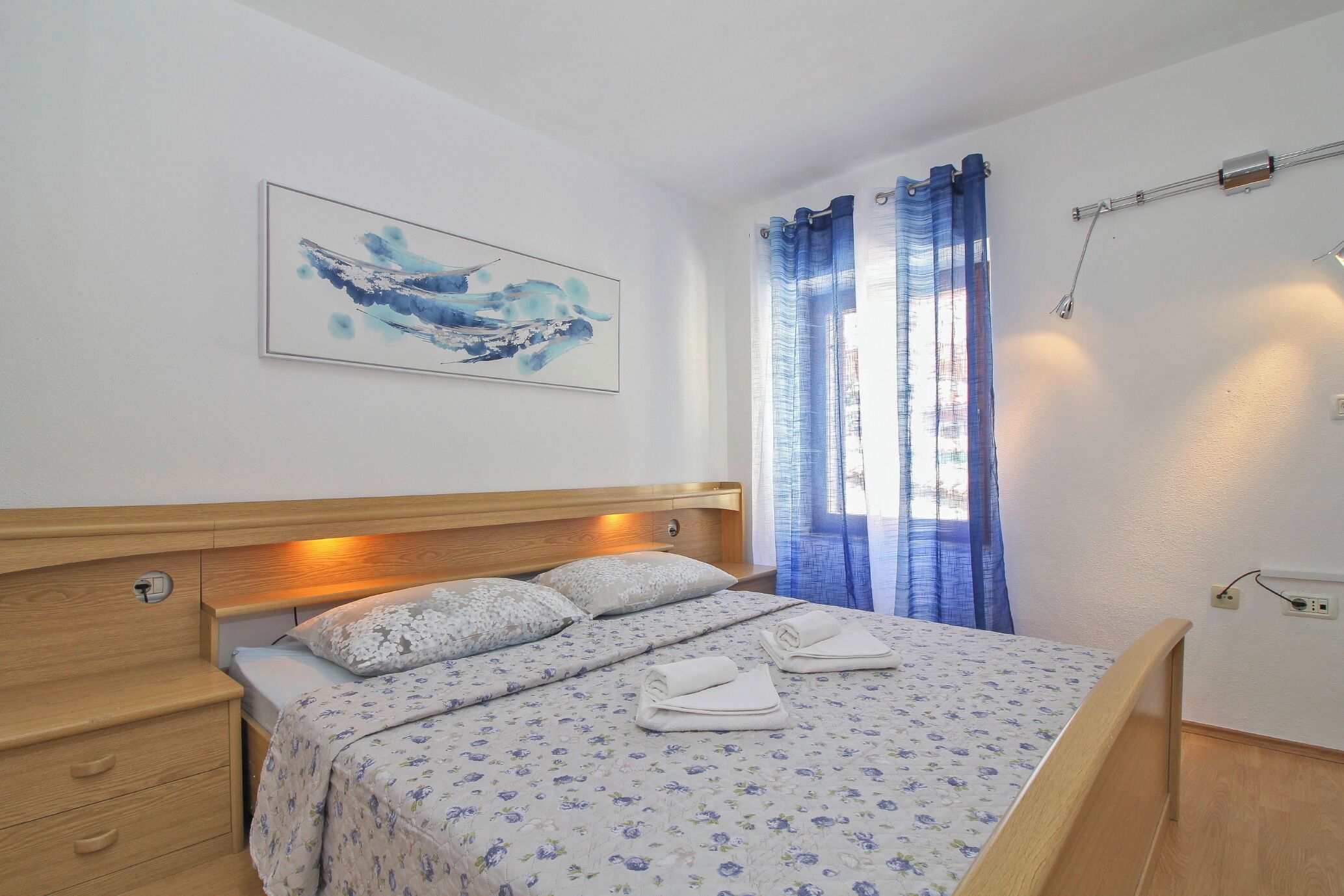 A neatly made bed with a floral bedspread, a wooden headboard, and a wall-mounted painting.