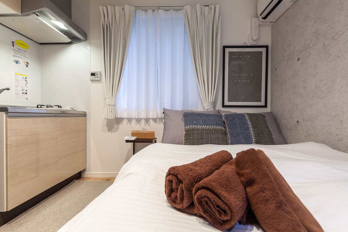 A hotel room with a bed, a small desk, a window with curtains, and a framed quote on the wall.