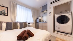 Habitación de hotel con cama, lavadora, microondas y una pequeña kitchenette.