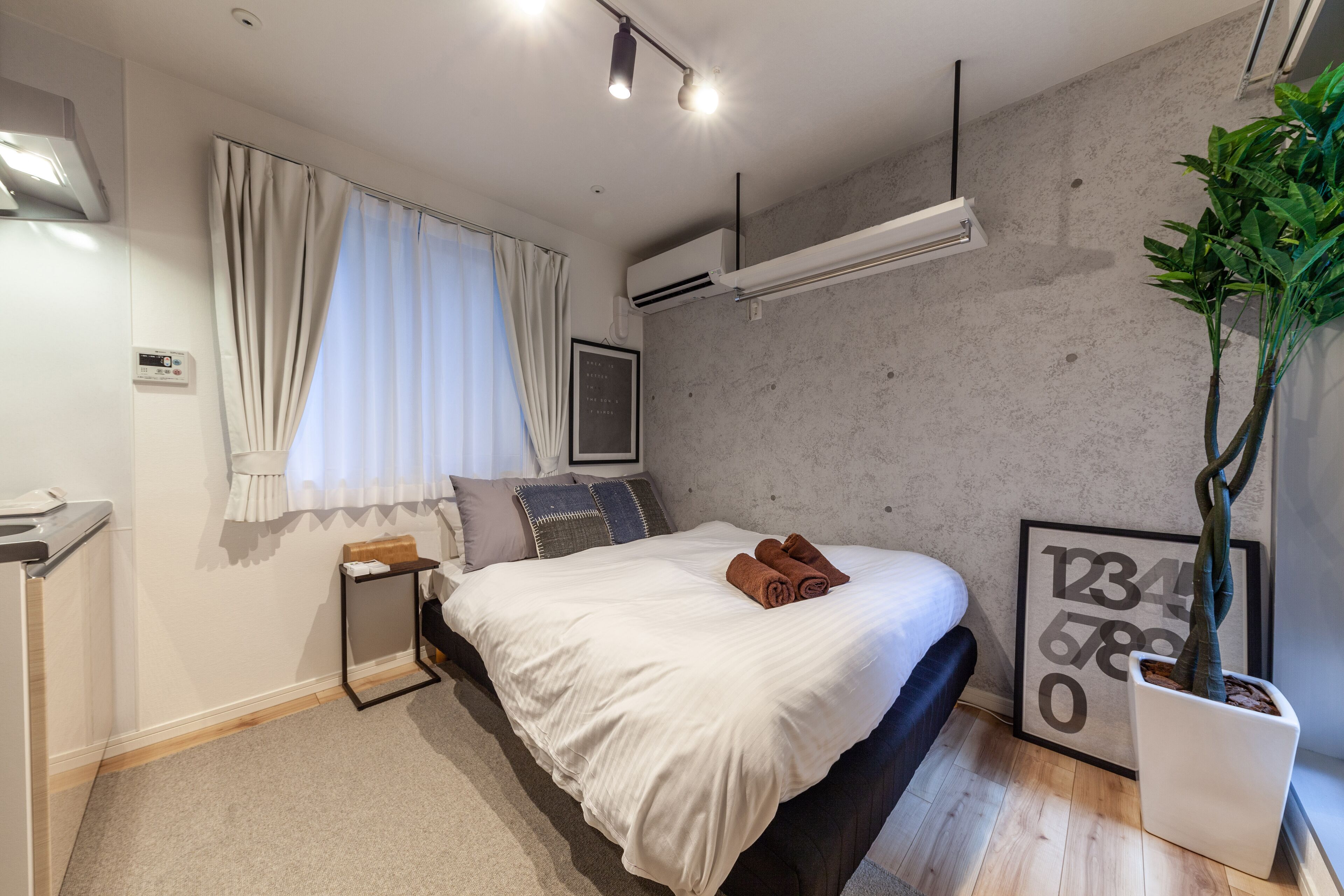 A modern bedroom with a bed, bedside table, air conditioning unit, and a potted plant.