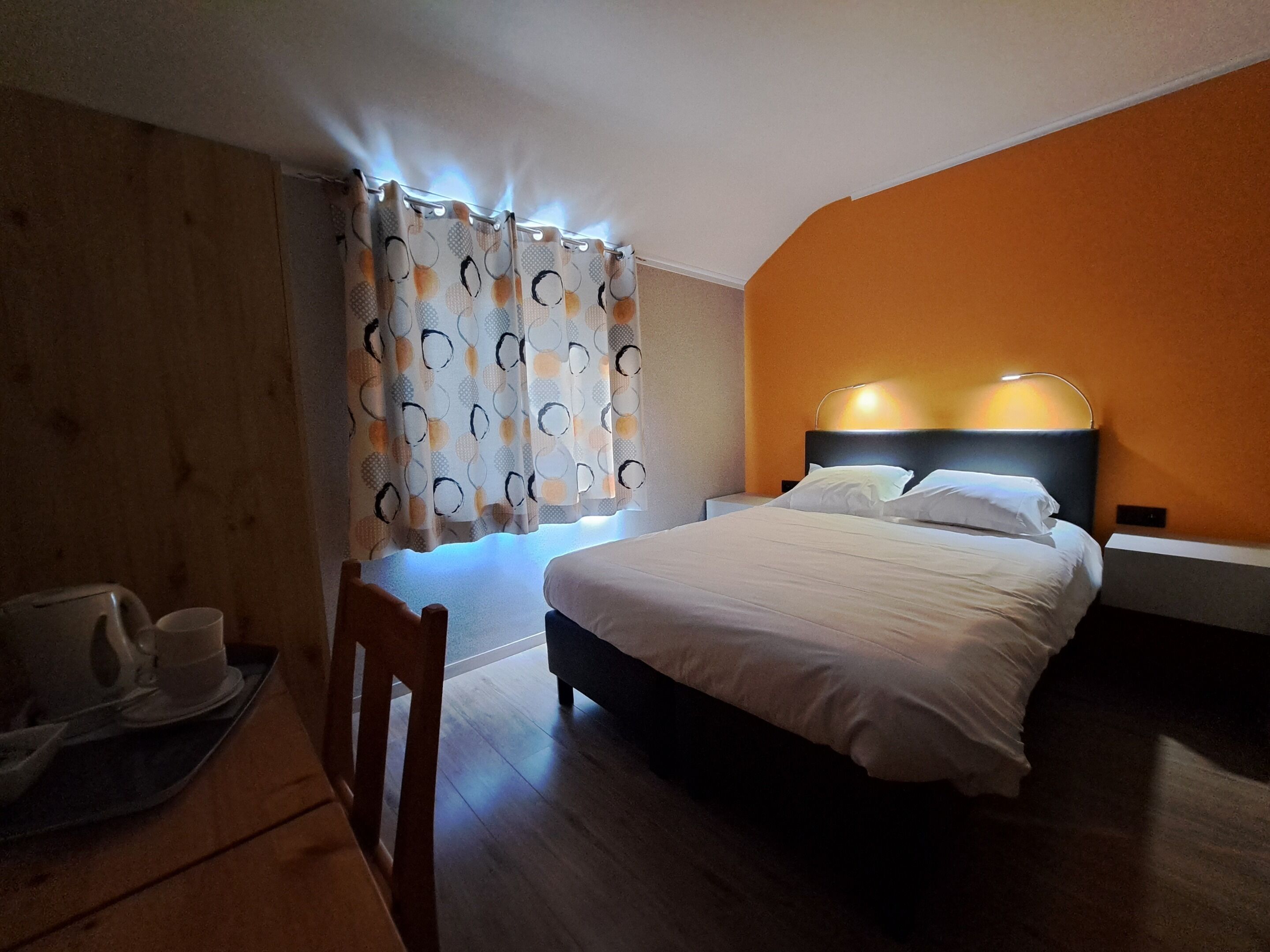 Una habitación de hotel con cama, mesita de noche, lámpara, silla y bandeja con tazas.