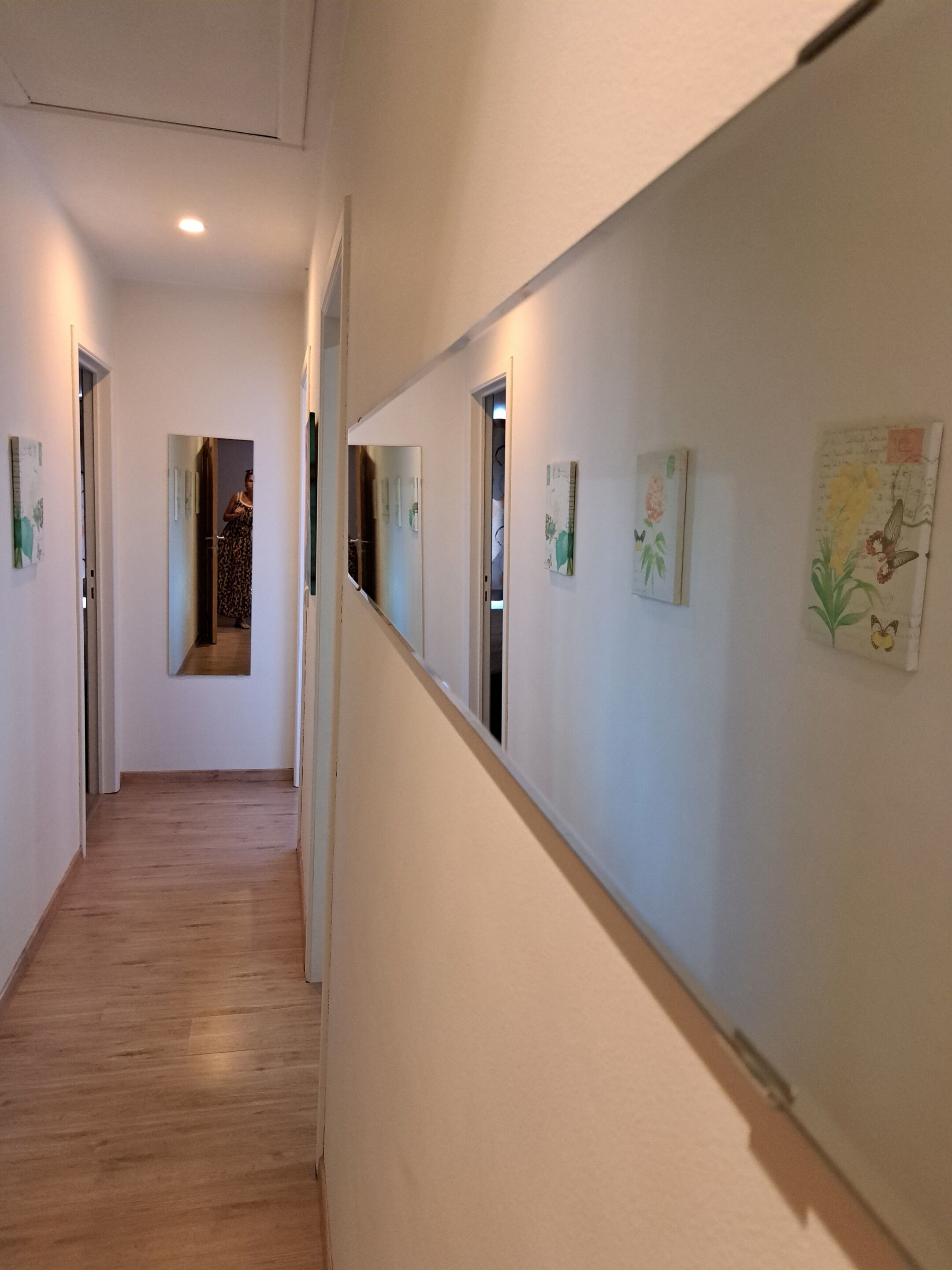 A hallway with wooden flooring, white walls, and several framed artworks.
