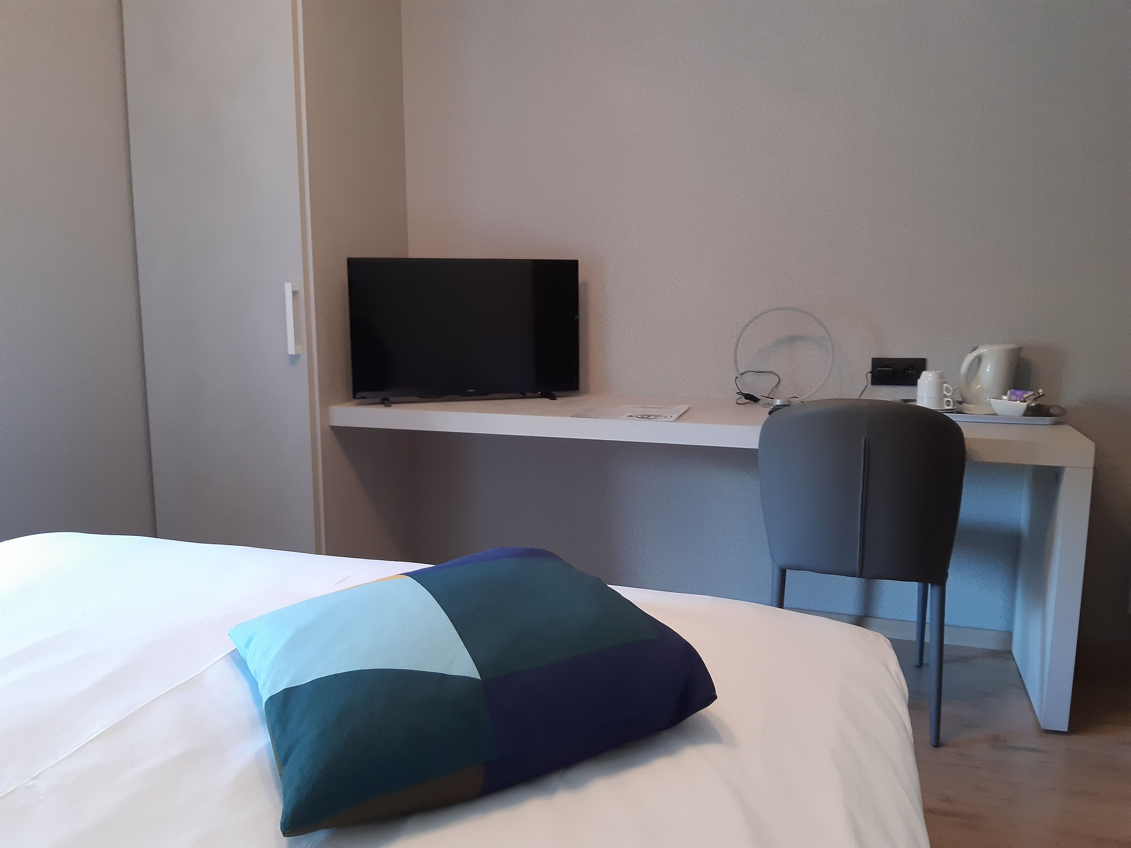 A hotel room with a bed, a desk, a chair, a television, and a coffee maker.