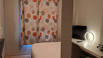 Une chambre à coucher avec un lit, un bureau avec un ordinateur et un miroir, et un rideau de douche à motifs à pois.