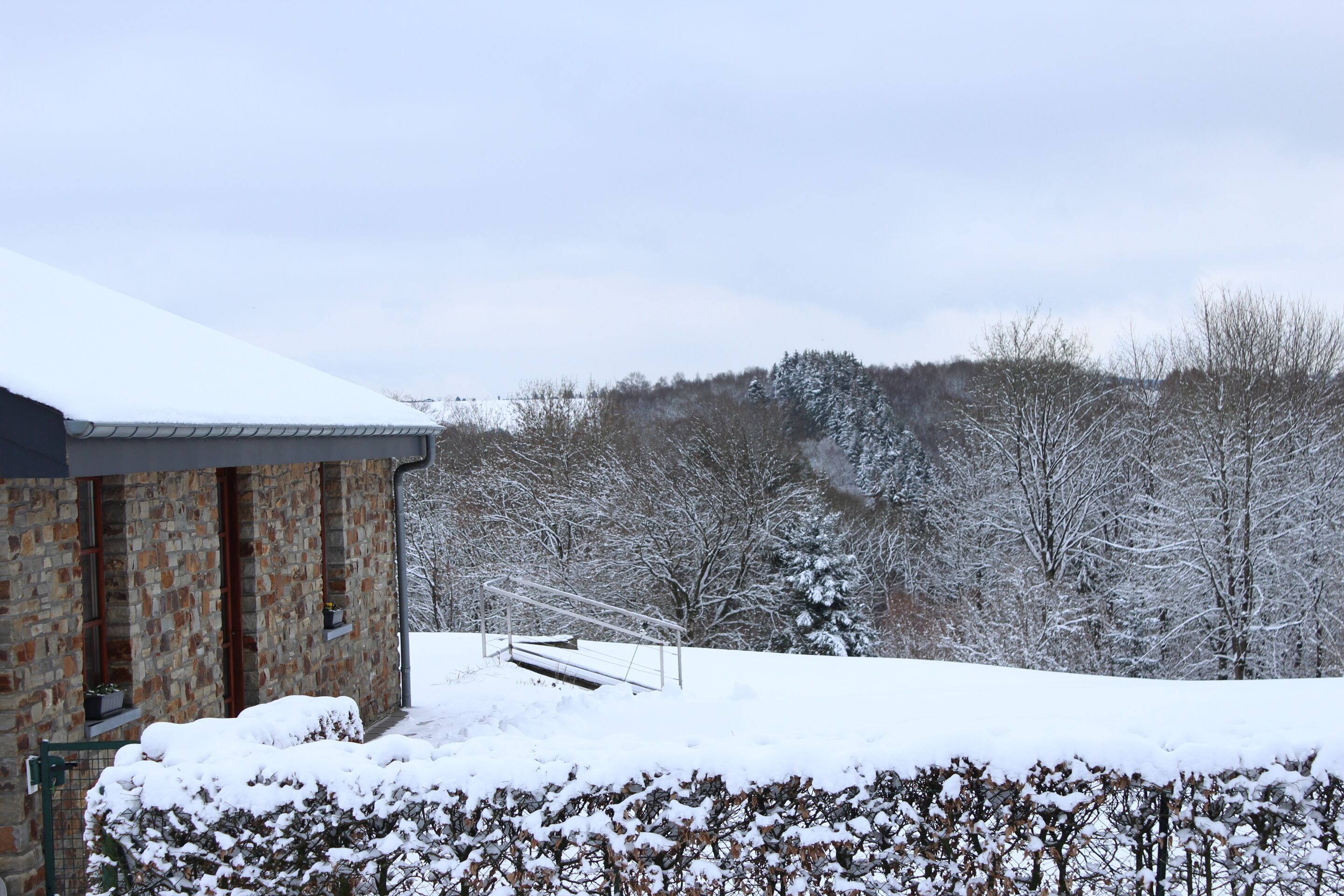 A stone building with a snow-covered roof and a metal gate.