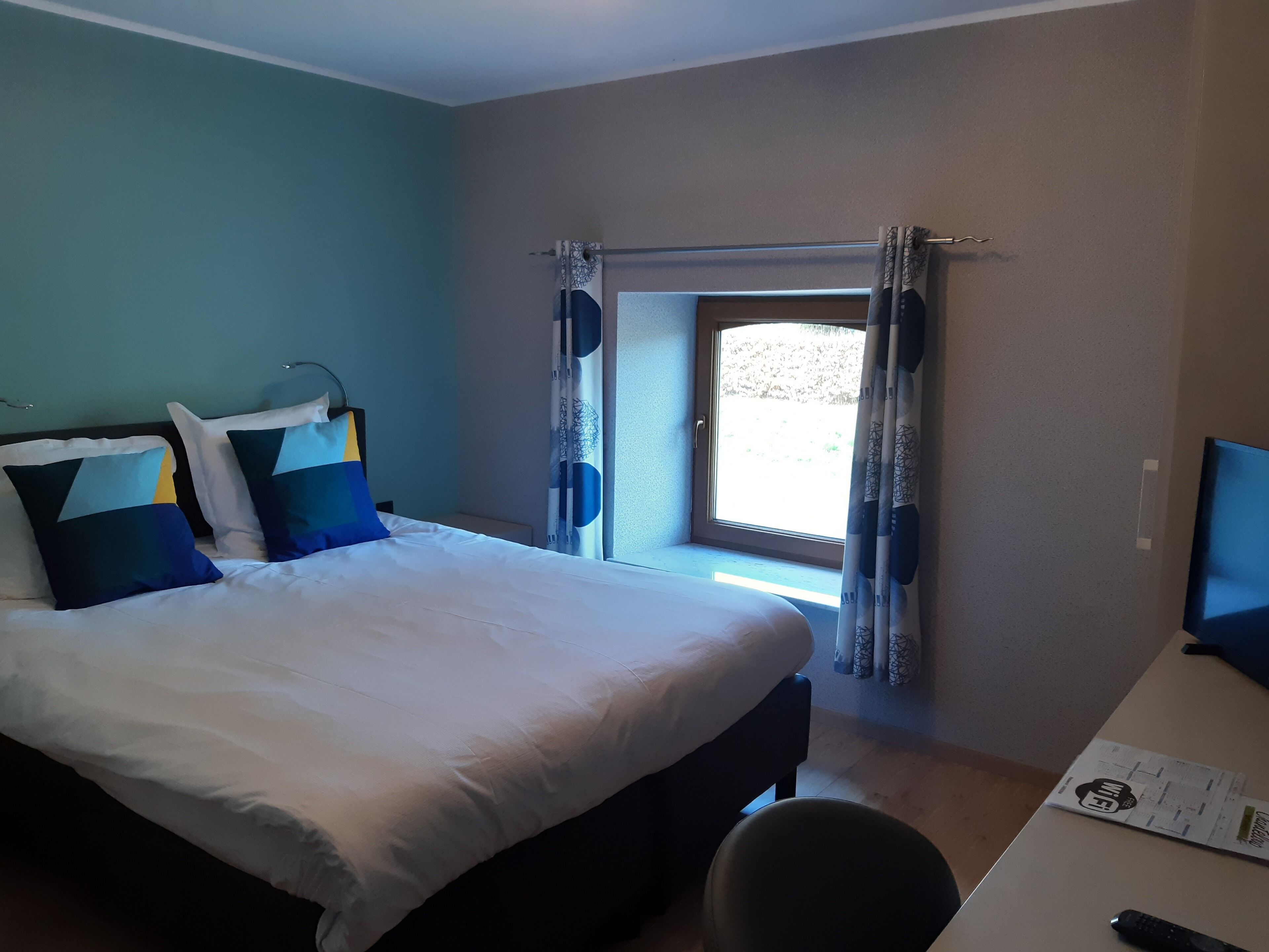 Une chambre d’hôtel avec un lit, un bureau et une fenêtre avec des rideaux.