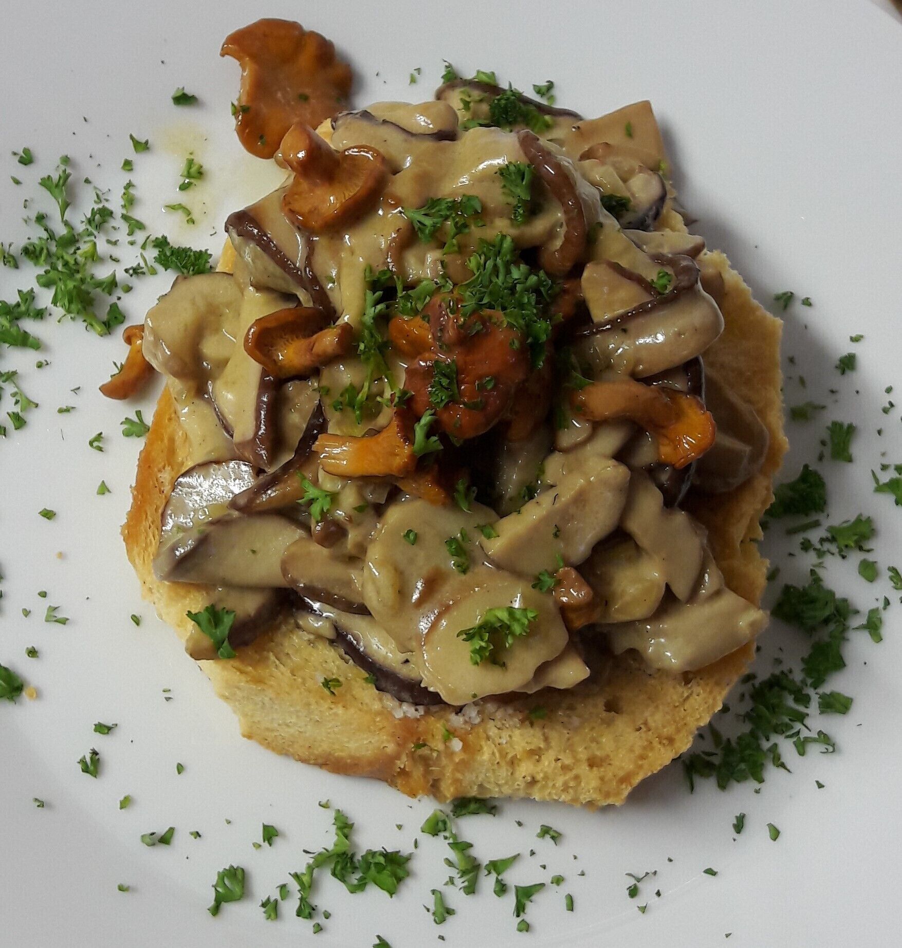 Een bord met plakjes champignons op een sneetje brood, versierd met gehakte peterselie.