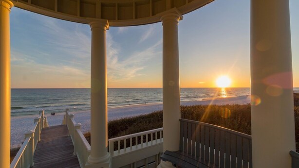 Une terrasse couverte offrant une vue sur la plage et l’océan au coucher du soleil.