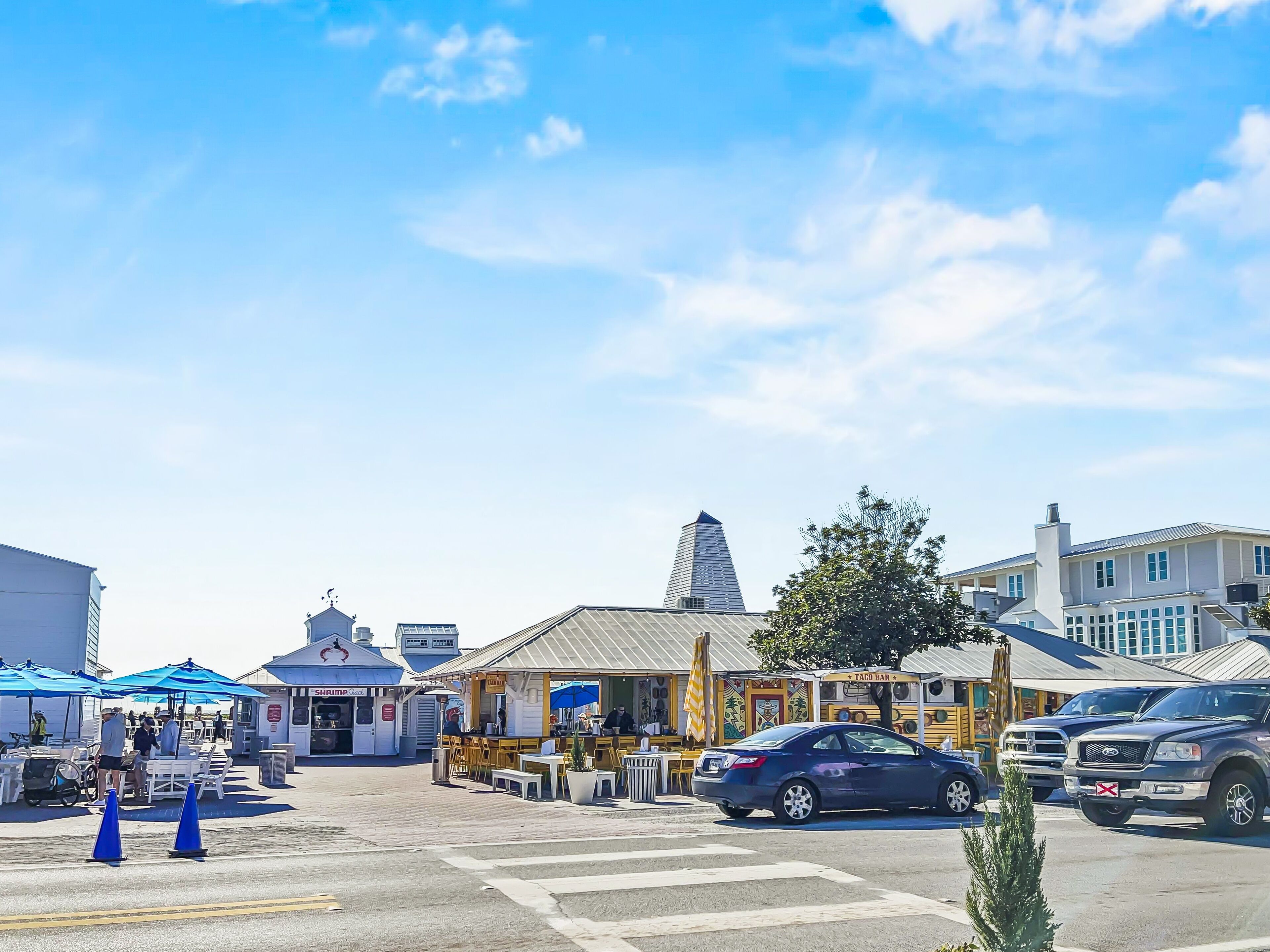 Una vista di strada con tavoli all'aperto presso un ristorante, un taco bar e un edificio con una torre caratteristica.