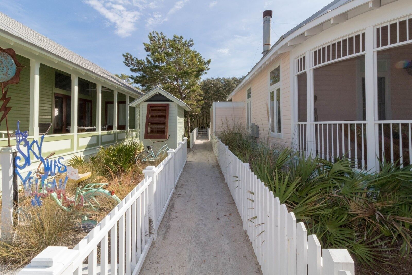 A narrow pathway flanked by two buildings with a white picket fence.