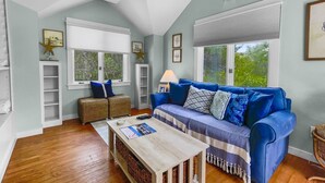 Un salon chaleureux avec un canapé bleu, une table basse en bois et des tables d’appoint en osier.