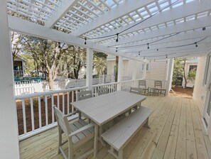 Um alpendre coberto com deck de madeira, guarda-corpos brancos e luzes de fada.