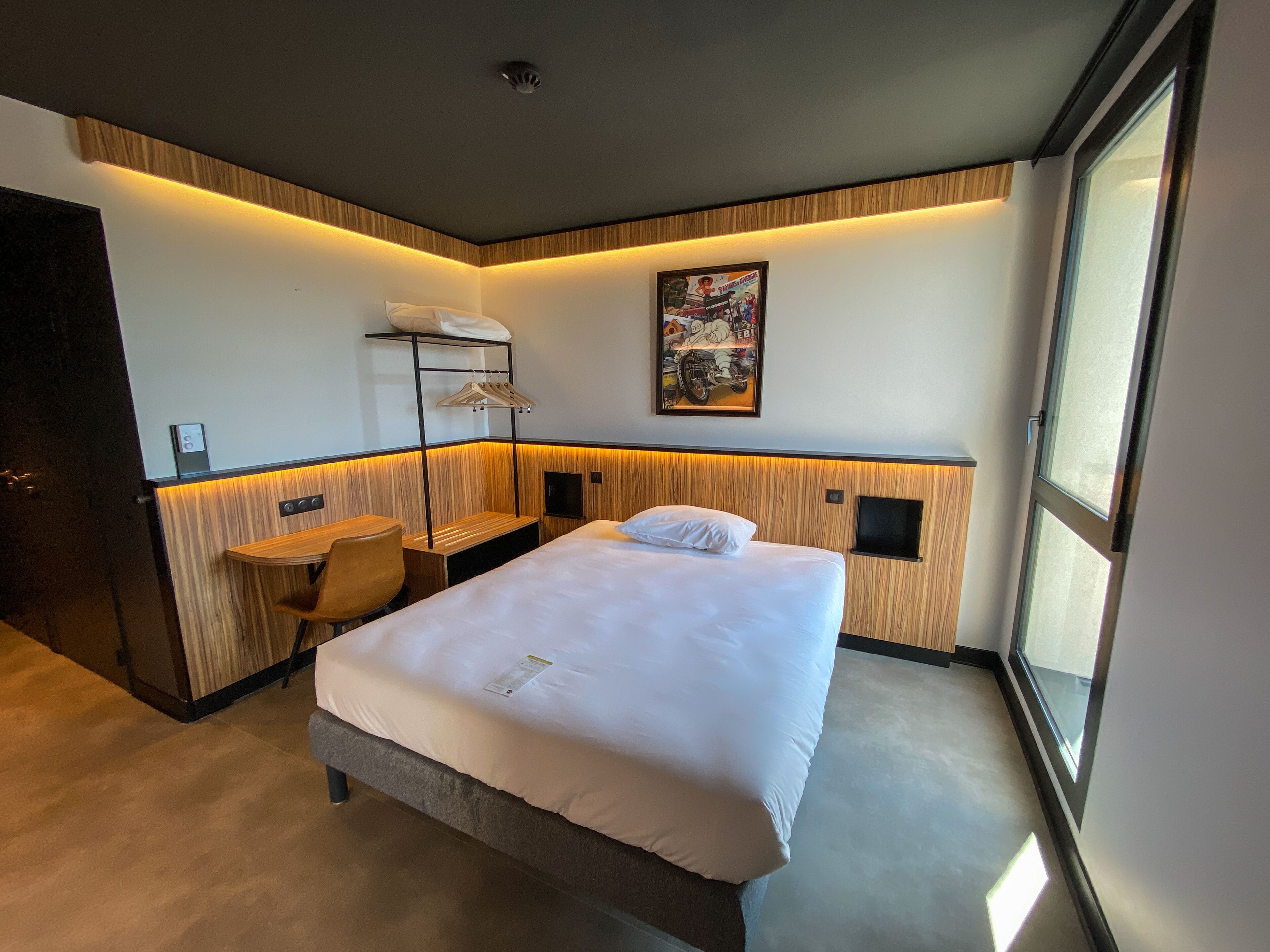 A hotel room with a bed, a desk, a chair, a TV, and a window.