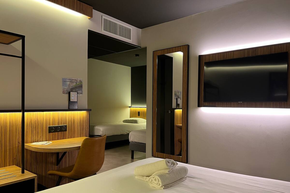 A hotel room with a bed, a desk, a chair, a TV, and a mirror.