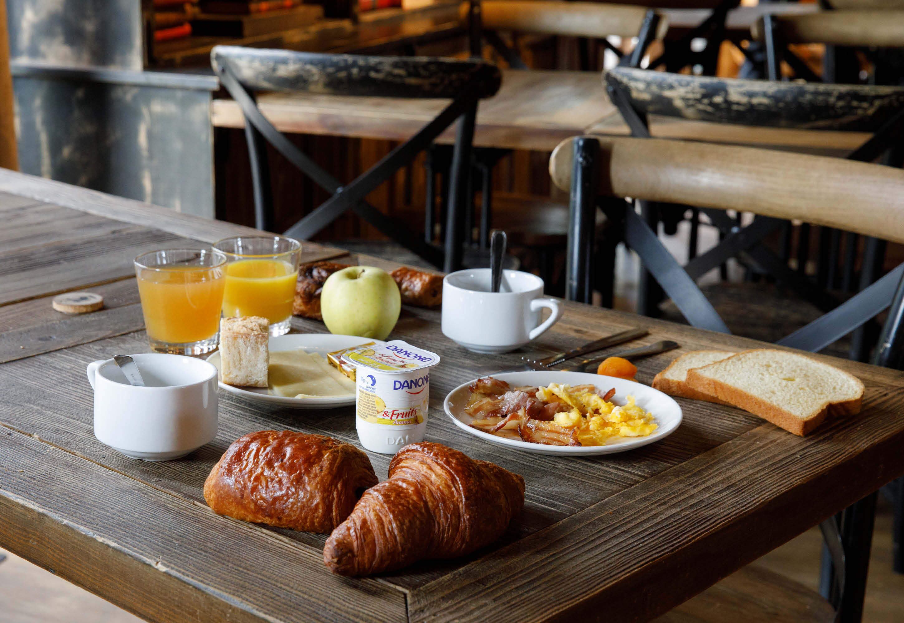 Una mesa de desayuno con cruasanes, jugo, yogur, tostadas y huevos.