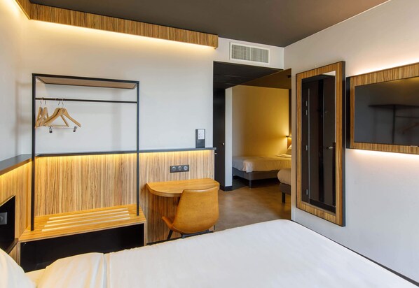 Una habitación de hotel moderna con cama, escritorio, silla, armario y espejo.