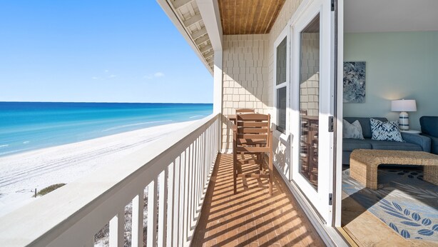 A balcony with a view of the beach, a wooden chair, and a sofa with a lamp.
