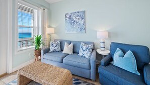 A living room with a blue sofa, two lamps, a blue abstract painting, and a potted plant.