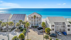 A beachfront hotel with multiple-story buildings, a parking area, and a view of the ocean.